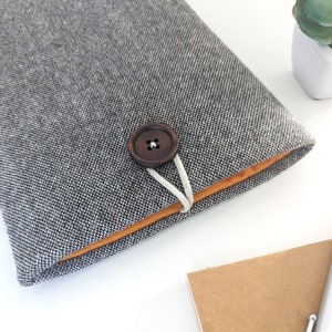 May include: A gray fabric notebook cover with a brown button closure and a light orange lining. The cover has a textured pattern.