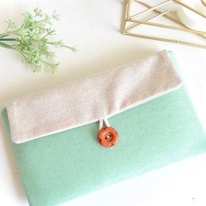 Könnte beinhalten: Eine hellgrüne Stofftasche mit einer beige Klappe und einem braunen Knopfverschluss.