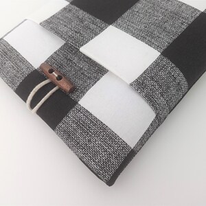 K&ouml;nnte beinhalten: Schwarze und wei&szlig;e karierte Stofftasche mit einem Verschluss aus Holz.