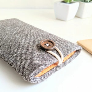 May include: A gray and orange fabric phone case with a brown button closure.