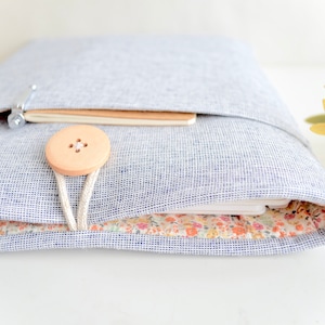 May include: A gray linen laptop sleeve with a floral lining and a wooden button closure. The sleeve is closed and a notebook is visible inside.