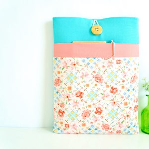May include: A turquoise and pink fabric laptop sleeve with a floral pattern and a wooden button closure.