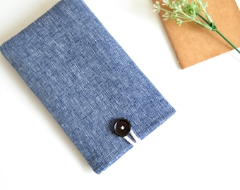 May include: A blue linen phone case with a white button and white stitching. The case is on a white surface.