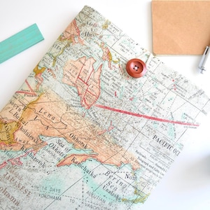 May include: A vintage-style notebook cover featuring a printed world map. The map is in shades of brown, blue and green, and includes text in Russian and English. A red button is attached to the cover.