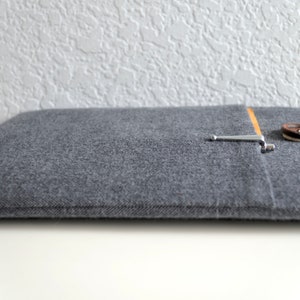 Peut inclure: Une housse pour ordinateur portable en feutre gris avec un bouton marron et une fermeture en m&eacute;tal argent&eacute;. La housse a une poche sur le devant avec une doublure en tissu beige.