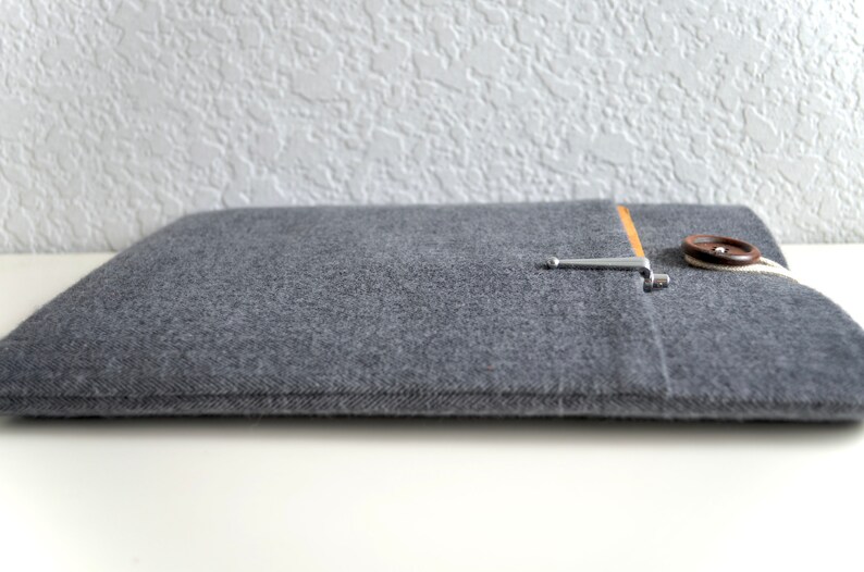 Peut inclure: Une housse pour ordinateur portable en feutre gris avec un bouton marron et une fermeture en m&eacute;tal argent&eacute;. La housse a une poche sur le devant avec une doublure en tissu beige.