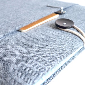 Puede incluir: Una funda para port&aacute;til azul claro con un patr&oacute;n de espiga. La funda tiene un cierre de madera y metal, un bot&oacute;n oscuro grande y un cord&oacute;n color crema. El interior es de color azul claro.