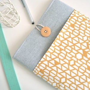 Puede incluir: Una funda para portátil gris y blanca con un patrón geométrico en tonos de amarillo y blanco. La funda tiene un cierre de solapa y un botón de madera.