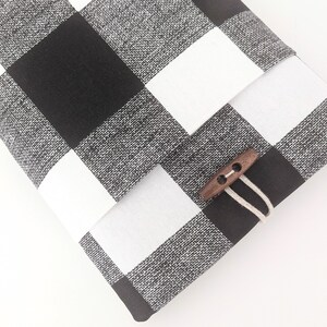 K&ouml;nnte beinhalten: Schwarze und wei&szlig;e karierte Laptop-H&uuml;lle aus Stoff mit einem Verschluss aus Holz.