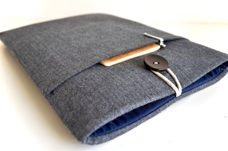 May include: A gray herringbone fabric laptop sleeve with a blue lining and a wooden flap closure. A black button and white string are visible.