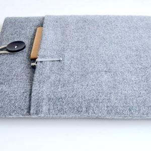 Puede incluir: Una funda gris para port&aacute;til hecha de tela texturizada con cierre de bot&oacute;n y un peque&ntilde;o bolsillo. La funda tiene un dise&ntilde;o simple y minimalista, adecuada para proteger un port&aacute;til o tableta.