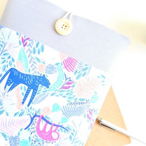 K&ouml;nnte beinhalten: Eine graue Laptoptasche mit wei&szlig;em Hintergrund und einem bunten Dschungel-Druck mit einem blauen Tiger, einem rosa Faultier und gr&uuml;nen Bl&auml;ttern. Die Tasche hat einen Knopfverschluss.