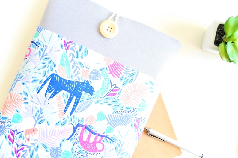 K&ouml;nnte beinhalten: Eine graue Laptoptasche mit wei&szlig;em Hintergrund und einem bunten Dschungel-Druck mit einem blauen Tiger, einem rosa Faultier und gr&uuml;nen Bl&auml;ttern. Die Tasche hat einen Knopfverschluss.