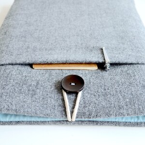 Puede incluir: Una funda gris para port&aacute;til con un patr&oacute;n de espiga, con un cierre de bot&oacute;n marr&oacute;n grande y un interior azul claro. La funda tiene un peque&ntilde;o acento de madera y un cierre met&aacute;lico.