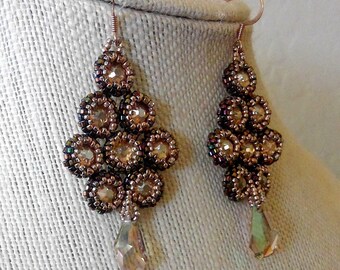 May include: A pair of dangle earrings with a teardrop crystal charm. The earrings are made with brown and gold beads and have a geometric design.