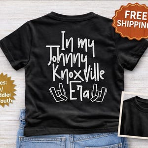 K&ouml;nnte beinhalten: Schwarzes T-Shirt mit dem wei&szlig;en Text "In my Johnny Knoxville Era" und einer Handgesten-Grafik. Erh&auml;ltlich in Baby-, Kleinkind- und Jugendgr&ouml;&szlig;en. Das Bild enth&auml;lt auch ein kleines Bild des Shirts.