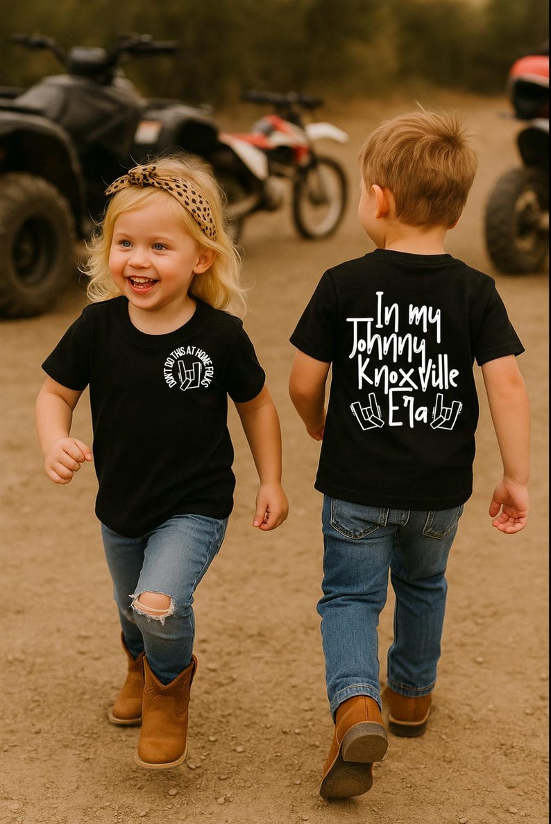 K&ouml;nnte beinhalten: Zwei Kinder in schwarzen T-Shirts und blauen Jeans gehen. Das erste Shirt hat den Text "DON'T DO THIS AT HOME FOLKS" mit einer Handgeste. Das zweite Shirt sagt "In my Johnny Knoxville Era" mit einer Handgeste auf der R&uuml;ckseite.