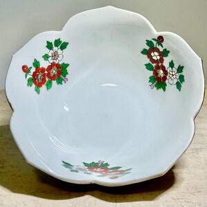 May include: White ceramic serving bowl with a scalloped edge and floral design. The bowl features red, white, and green flowers. The rim has a gold trim. A decorative piece for serving food.