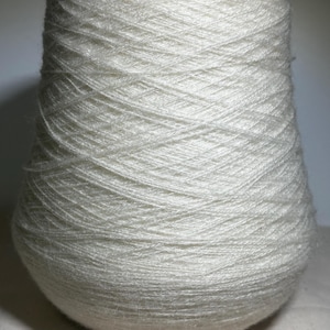May include: A large cone of off-white yarn. The yarn is tightly wound, creating a textured surface. The cone shape tapers from a wider base to a narrower top. The yarn appears soft and fluffy, suitable for knitting or crocheting projects.