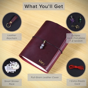 May include: A dark red leather journal with the name Mary engraved on the cover, secured by a black elastic cord with a bead charm. Included are a leather keychain, three metal charms, a sticker pack, and an extra red elastic cord.