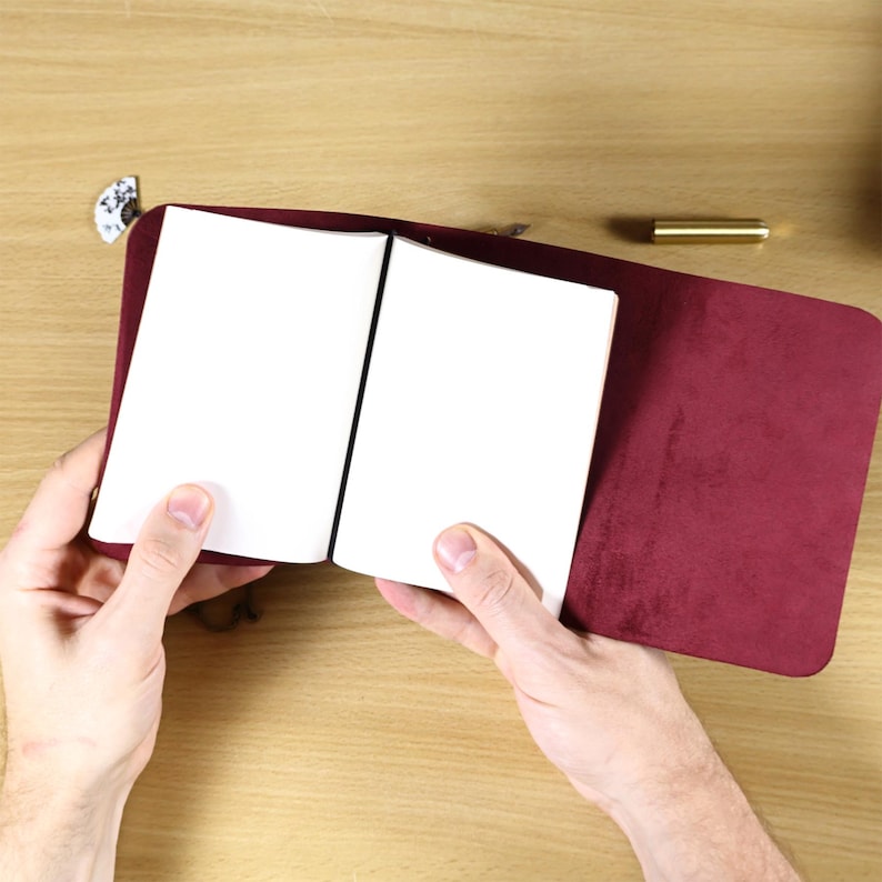 May include: A deep burgundy notebook cover with a soft, suede-like texture, holding two open white paper inserts. The cover features rounded corners and a smooth, matte finish, providing a simple and functional design for organizing loose pages.