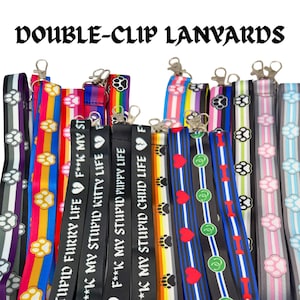 May include: A collection of double-clip lanyards featuring various colorful patterns, including paw prints, hearts, and bones. Several black lanyards display the white text F**K MY STUPID FURRY LIFE, F**K MY STUPID KITTY LIFE, and F**K MY STUPID PUPPY LIFE.