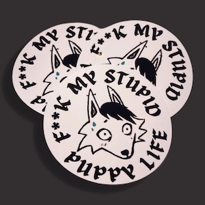 May include: A stack of white, circular stickers with a black and white cartoon dog illustration. The stickers have the phrases "F**k my stupid life" and "Puppy Life" printed in black, stylized font around the dog's head.