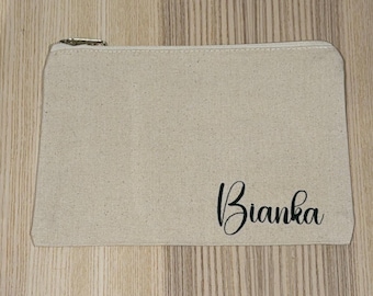 May include: A beige canvas zippered pouch with the name "Bianka" printed in black cursive script. The pouch has a rectangular shape and a metal zipper.