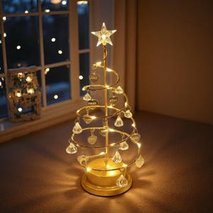Könnte beinhalten: Eine goldfarbene, spiralförmige Weihnachtsbaumdekoration aus Metall mit einem Stern an der Spitze, beleuchtet durch integrierte warmweiße LED-Lichterketten. Die Struktur ist mit hängenden, kristallartigen Ornamenten und herzförmigen Anhängern versehen.