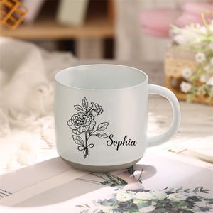 May include: White ceramic mug with a black line drawing of flowers and the name "Sophia" printed on the side.