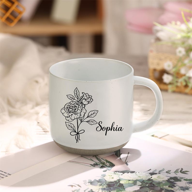 May include: White ceramic mug with a black line drawing of flowers and the name "Sophia" printed on the side.