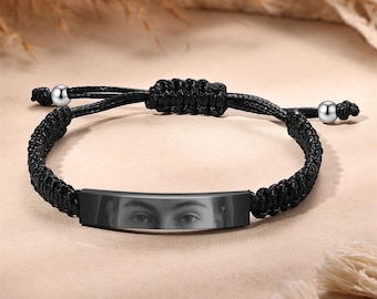 May include: Black braided bracelet with a silver metal bar featuring a black and white photo of a person's eyes.
