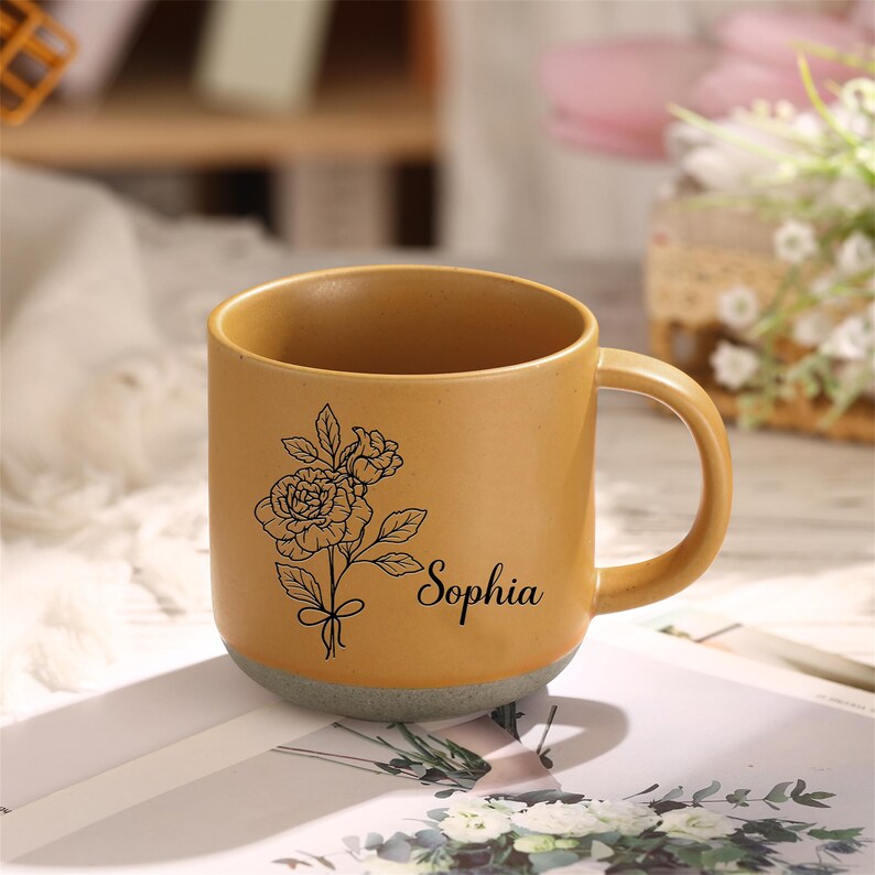 May include: A yellow ceramic mug with a black floral design and the name "Sophia" printed on the side.