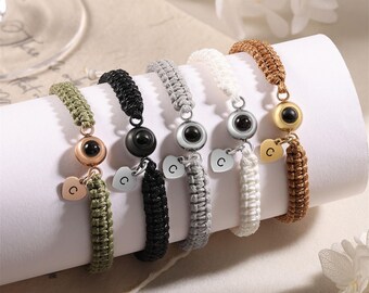 May include: Five braided bracelets with a small heart charm and a black eye bead. The bracelets are in green, black, gray, white, and brown.