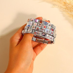 Könnte beinhalten: Ein silberfarbenes Gliederarmband mit mehreren rechteckigen und herzförmigen Anhängern, die jeweils ein einzigartiges, kleines Farbfoto zeigen. Die Metallglieder sind zu einem flexiblen, dehnbaren Band miteinander verbunden.