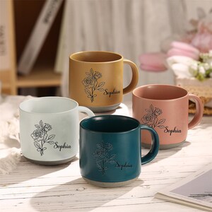 May include: Four ceramic mugs with floral designs and the name "Sophia" printed on each. The mugs are in different colors: white, light brown, pink, and teal.