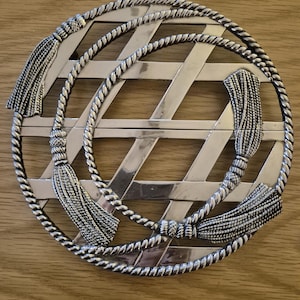 May include: Silver-toned round hot pad with a woven design and four tassels.