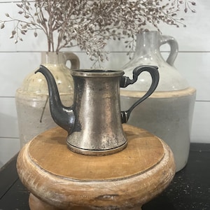 May include: A white ceramic mug with a black handle and the text "But First, Coffee" in a black, bold font. The mug is sitting on a wooden surface. The mug is approximately 4 inches tall.