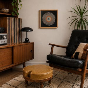 Może przedstawiać: Salon w stylu mid-century modern. Prezentuje oprawione dzieło sztuki z okrągłym wzorem w odcieniach pomarańczu, błękitu i szarości. Pokój obejmuje czarny skórzany fotel, drewnianą szafkę z gramofonem i okrągłą pufę.
