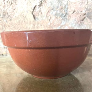 May include: A large, brown ceramic mixing bowl. The bowl has a smooth, rounded surface and a slightly flared rim.
