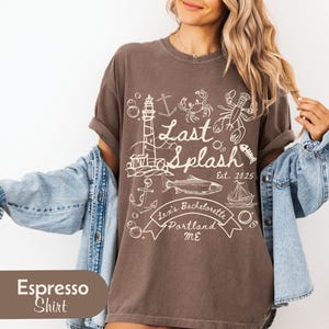 May include: Espresso-colored t-shirt with a white nautical-themed graphic. The design includes a lighthouse, anchors, fish, lobster, and the text "Last Splash Est. 2025, Lexi's Bachelorette, Portland ME."