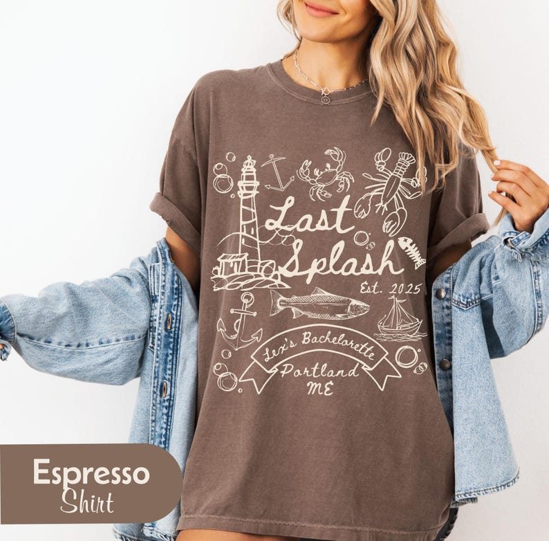 May include: Espresso-colored t-shirt with a white nautical-themed graphic. The design includes a lighthouse, anchors, fish, lobster, and the text "Last Splash Est. 2025, Lexi's Bachelorette, Portland ME."