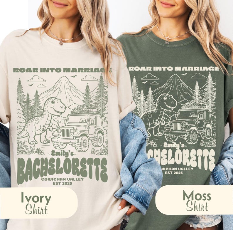 Op de afbeelding: Een ivoorkleurig en een mosgroen t-shirt, elk met een grafische print van een dinosaurus, een terreinwagen, bergen en bomen. De tekst luidt ROAR INTO MARRIAGE, Emily's BACHELORETTE, COWICHAN VALLEY en EST 2025 in een retro lettertype.