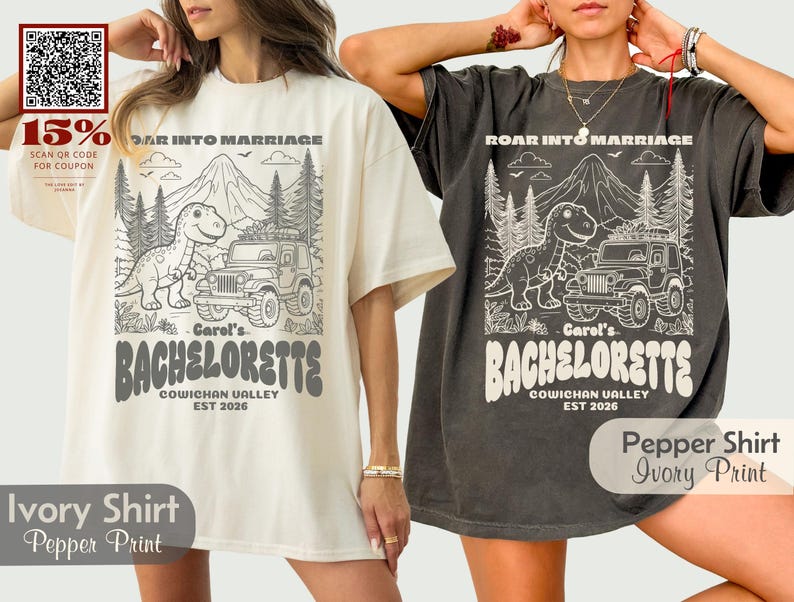 Op de afbeelding: Twee oversized t-shirts, &eacute;&eacute;n ivoorkleurig en &eacute;&eacute;n antracietgrijs, elk met een grafische print van een dinosaurus, een jeep, bergen en dennenbomen. De tekst luidt ROAR INTO MARRIAGE, Carol's BACHELORETTE, COWICHAN VALLEY en EST 2026.