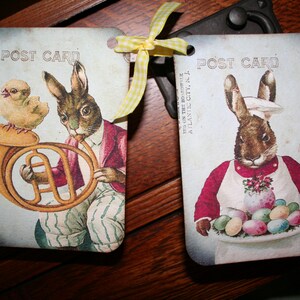 May include: Two vintage postcard style images with a bunny rabbit theme. The first image features a brown bunny rabbit holding a french horn with a yellow chick beside it. The second image features a brown bunny rabbit wearing a chef's hat and apron holding a plate of colorful Easter eggs. Both images have the text "POST CARD" printed on them.