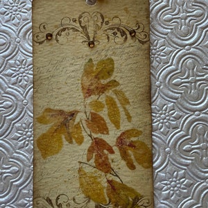 May include: A vintage-style bookmark featuring a pressed leaf design. The bookmark is decorated with a brown ribbon and has a distressed, aged look. The background features handwritten script.