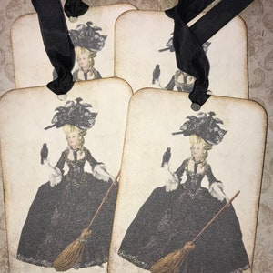 May include: Four rectangular tags with rounded corners, each featuring a vintage illustration of a woman in a black gown, holding a broom and a bird. The tags are tied together with a black ribbon.