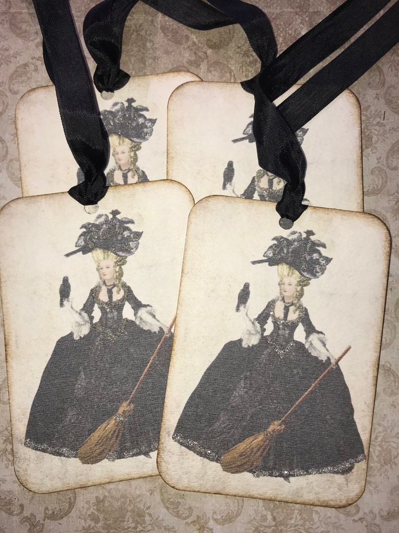May include: Four rectangular tags with rounded corners, each featuring a vintage illustration of a woman in a black gown, holding a broom and a bird. The tags are tied together with a black ribbon.