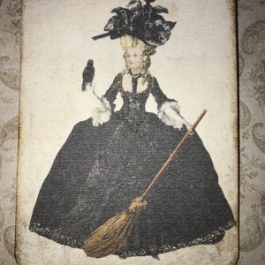 May include: A rectangular wooden ornament featuring a vintage illustration of a woman in a black gown and elaborate hat, holding a broom and a bird. The image has a distressed, aged appearance, with a black ribbon for hanging.