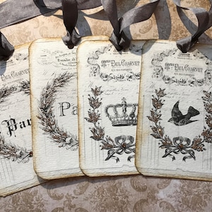 May include: Four vintage-style gift tags with black and white illustrations and gold glitter accents. The tags feature a crown, a bird, and a wreath. The text on the tags reads "St. Paul Charvet".
